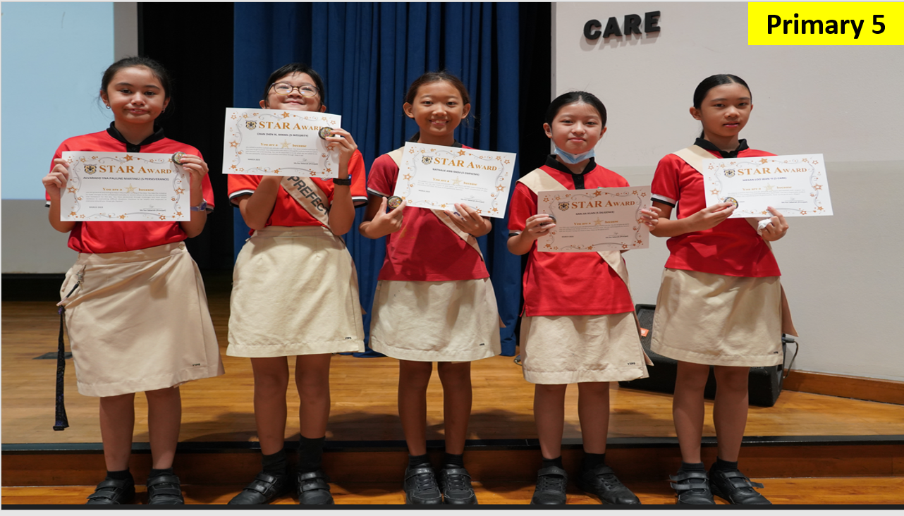 Five Primary 5 girls in red uniforms stand on a stage holding Star Award certificates.